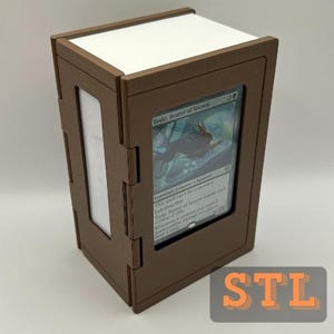 Könnte beinhalten: Eine braune und weiße Kartenaufbewahrungsbox mit einer Karte auf der Vorderseite. Die Karte zeigt ein Bild einer Kreatur und den Text "Toski, Bearer of Secrets". Die Box hat eine rechteckige Form und besteht aus einem starren Material.