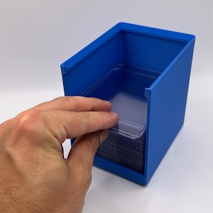 May include: A blue plastic card holder with a stack of clear card sleeves inside. The holder is rectangular with angled sides. A hand is shown inserting a card sleeve into the holder.
