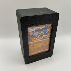 May include: A black plastic card holder with a clear window to display a Pokemon trading card. The card features a Machop evolution, Machamp, with the text "Evolves from Machoke" and "Lost Origin". The card has a red, orange, and yellow color scheme.