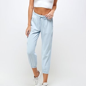 May include: A light blue pair of casual pants with a drawstring waist and cuffed legs. The pants are made of a soft, lightweight fabric and are perfect for everyday wear.