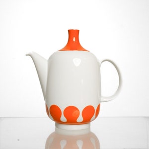 May include: A white ceramic teapot with an orange lid and orange accents around the bottom. The teapot has a rounded body and a spout on one side and a handle on the other.