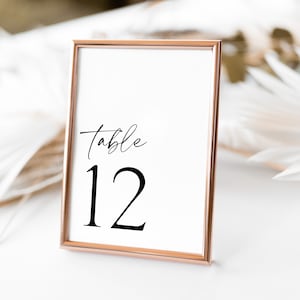 May include: A rose gold table number frame with a white card that says "table 12" in black calligraphy.