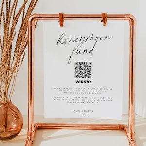 Pode incluir: Um cartaz branco com texto preto que diz "honeymoon fund" e um código QR com a palavra "venmo" abaixo. O cartaz está em uma moldura de tubo de cobre.