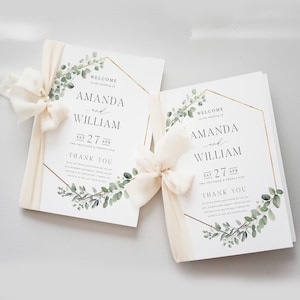 May include: Two wedding programs with the names "Amanda and William" printed in black, accented with gold geometric frames and greenery. Each program is tied with a cream-colored ribbon. The date "Sat 27 Apr" is also printed on the program.