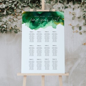 May include: A green and gold watercolor seating chart with the text "find your seat" and a list of names and table numbers. The chart is on an easel.