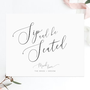 May include: A white card with black calligraphy that reads "Sip and be Seated" with the words "Much Love" and "The Bride & Groom" below.