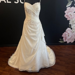 Puede incluir: Un vestido de novia de satén blanco con escote de corazón y un corpiño ajustado. El vestido tiene una falda de capas con una superposición de tul y delicados abalorios en todo.
