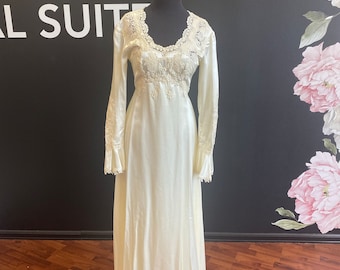 May include: A white satin wedding dress with long sleeves and lace detailing. The dress has a scoop neckline and a fitted bodice. The skirt is full and flowing.