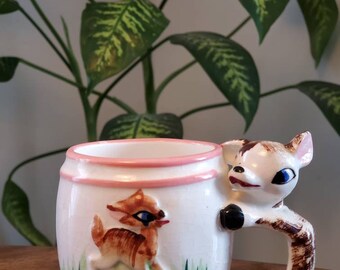 May include: A white ceramic mug with a pink rim and a deer handle. The mug features a cartoon deer with brown spots and green grass. The text "ALWAYS DRINK MILK" is printed on the bottom of the mug.
