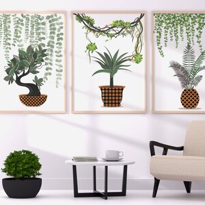 Pode incluir: Três impressões emolduradas de plantas em vasos com videiras penduradas. As impressões estão penduradas em uma parede branca acima de uma mesa de café branca com uma xícara de café e livros. Uma poltrona bege com pernas pretas fica na frente da mesa. Um abajur preto está no fundo.