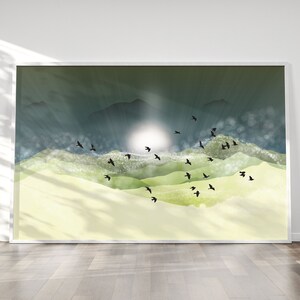 May include: A framed art print depicting a sunrise over a mountainous landscape. The artwork uses green, yellow, and blue hues, with black birds in silhouette. The print is displayed on a white wall.