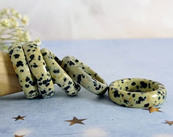 May include: A set of five rings made of dalmatian jasper, a light green stone with black spots. The rings are stacked on top of each other, with the largest ring at the bottom and the smallest ring at the top.