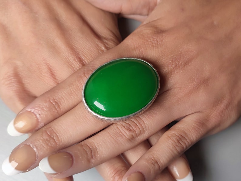 Pode incluir: Um anel de prata com uma grande gema verde oval.