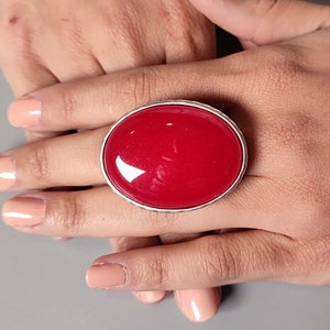 May include: A large, oval-shaped ring with a bright red, glossy stone set in a silver-toned metal band.