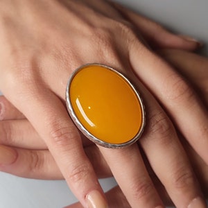 Könnte beinhalten: Ein silberner Ring mit einem großen, ovalen, leuchtend gelben Edelstein.