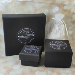 Pode incluir: Tr&ecirc;s caixas pretas com tampas, cada uma com um adesivo circular branco que diz "Handmade by Corky and Stoner. With love." As caixas est&atilde;o sobre uma superf&iacute;cie marrom claro.
