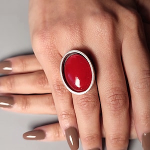 Op de afbeelding: Een zilveren ring met een grote, ovale rode steen.