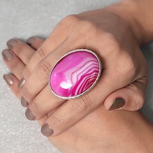 May include: A silver ring with a large oval pink and white agate gemstone. The gemstone has a swirling pattern.