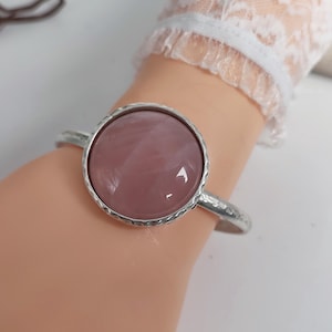 May include: A silver bangle bracelet with a large, round, pink gemstone cabochon.