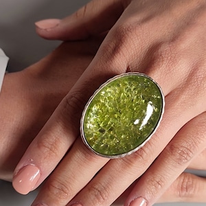 May include: A silver ring featuring a large oval green gemstone. The gemstone has a sparkly, textured surface.