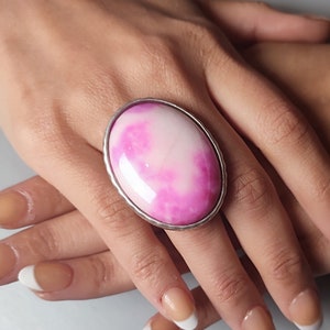 Peut inclure: Une grande bague ovale avec un motif en spirale rose et blanc. La bague est sertie d'argent et a une finition lisse et polie.