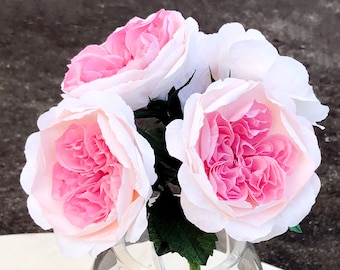 Puede incluir: Un ramo de rosas de papel rosa y blanco en un jarrón de vidrio transparente. Las rosas están dispuestas en un racimo y tienen un aspecto delicado y arrugado.