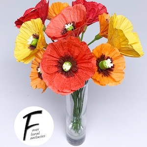 May include: A vibrant bouquet of paper poppies in a clear glass vase. The flowers are in shades of red, orange, and yellow, with green stems and white centres. The image includes the text "faux floral fantasies".