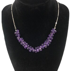 May include: A silver chain necklace with a row of faceted amethyst beads. The beads are a deep purple color and are arranged in a staggered pattern.