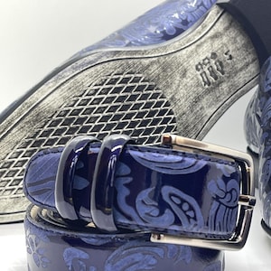 May include: A close-up of a navy blue belt with a silver buckle. The belt features a glossy finish and a repeating floral pattern. The image also shows a matching shoe with a similar design.