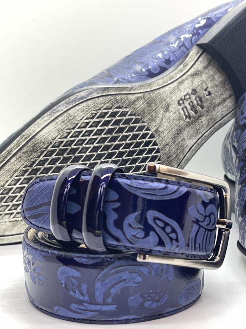 May include: A close-up of a navy blue belt with a silver buckle. The belt features a glossy finish and a repeating floral pattern. The image also shows a matching shoe with a similar design.