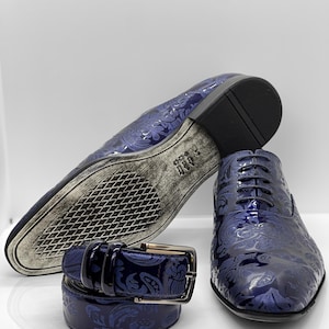May include: A set of men's formal wear accessories, including a pair of blue dress shoes, a matching belt, and the sole of a second shoe. The shoes and belt feature a floral pattern.