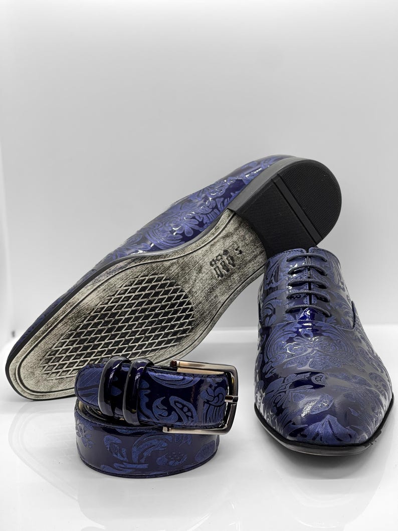 May include: A set of men's formal wear accessories, including a pair of blue dress shoes, a matching belt, and the sole of a second shoe. The shoes and belt feature a floral pattern.
