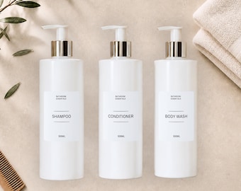 May include: Three white bathroom essential bottles with silver pump tops labeled "Shampoo", "Conditioner", and "Body Wash". Each bottle holds 500mL. A comb, a towel, and greenery are in the background.