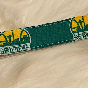 May include: Green and yellow fabric keychain with a Seattle basketball team logo and a silver key ring.