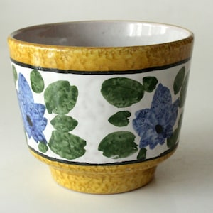 Puede incluir: Una maceta de cerámica amarilla con fondo blanco y diseño floral azul y verde.
