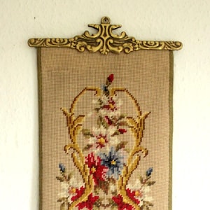Könnte beinhalten: Ein antiker Wandbehang aus Nadelfilz mit einem floralen Muster, gerahmt in einem goldenen Metallrahmen. Das Design zeigt einen Strauß roter, weißer und blauer Blumen mit grünen Blättern.