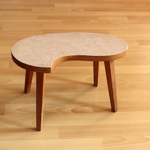 May include: A wooden side table with a unique crescent-shaped top. The table has three legs and is made of light brown wood.