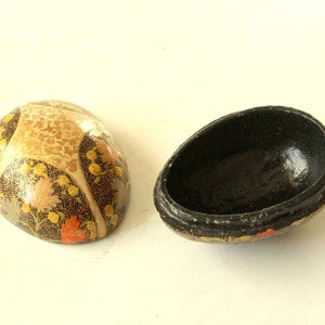 Può includere: Una scatola decorativa a forma di uovo con un interno nero e un design floreale colorato all'esterno. La scatola è realizzata in cartapesta ed è un'artigianato tradizionale indiano.