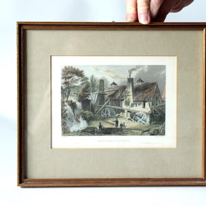May include: Framed vintage print depicting a rural scene with a water mill, trees, and figures. The print is in a wooden frame with a neutral mat. The artwork features a detailed illustration with muted colors and a classic aesthetic.