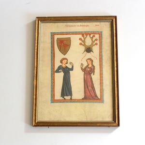 May include: A framed medieval-style illustration featuring two figures in long robes, one in blue and one in red, positioned below a shield and a branched crest. The artwork is enclosed in a thin gold frame with a decorative border around the central scene.