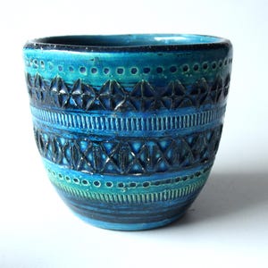 Op de afbeelding: Een keramische vaas met een textuur en een levendig kleurenpalet van blauw en groen. De vaas heeft geometrische patronen en een cilindrische vorm, geschikt voor interieurdecoratie.