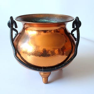 Può includere: Una pentola di rame con tre gambe e due manici in ferro nero. La pentola ha una finitura martellata ed è in stile tradizionale.