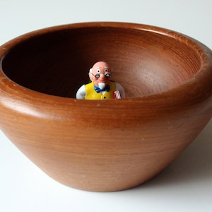 Könnte beinhalten: Eine Holzschale mit einer kleinen Plastikfigur eines Mannes mit Brille und gelber Weste im Inneren.