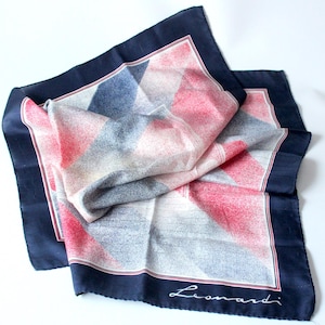 May include: A folded silk scarf with a geometric pattern in red, white, and blue. The scarf has a navy blue border with a thin red and white stripe. The brand name "Leonardi" is written in cursive in the corner.