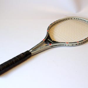 Könnte beinhalten: Ein weißer und schwarzer Tennisschläger mit schwarzem Griff. Der Schläger hat rote Akzente am Rahmen.