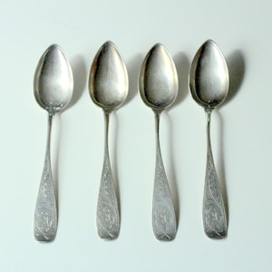 Peut inclure: Quatre cuillères en argent avec des motifs ornés sur les manches. Les cuillères sont disposées en rangée, les cuillères face au spectateur.