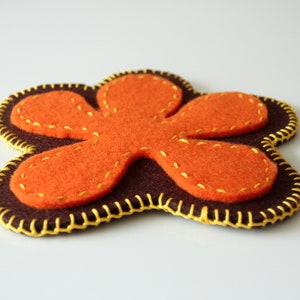 Può includere: Un fiore di feltro marrone con petali di feltro arancioni e cuciture gialle. Il fiore è un design semplice a cinque petali.