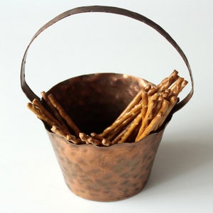 May include: A hammered copper bowl with a handle, filled with pretzel sticks.