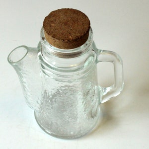 Könnte beinhalten: Transparente Teekanne aus Glas mit strukturierter Oberfläche und Griff. Die Teekanne hat einen Korken. Die Teekanne ist leer und bereit, mit Tee oder anderen Flüssigkeiten gefüllt zu werden.