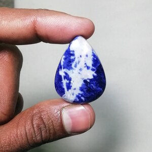 May include: A teardrop-shaped cabochon gemstone with a blue and white marbled pattern. The stone is polished and has a smooth surface.